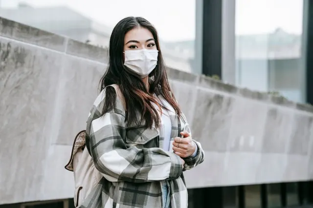 Woman in a checked coat standing in front of a concrete wall, before background removal